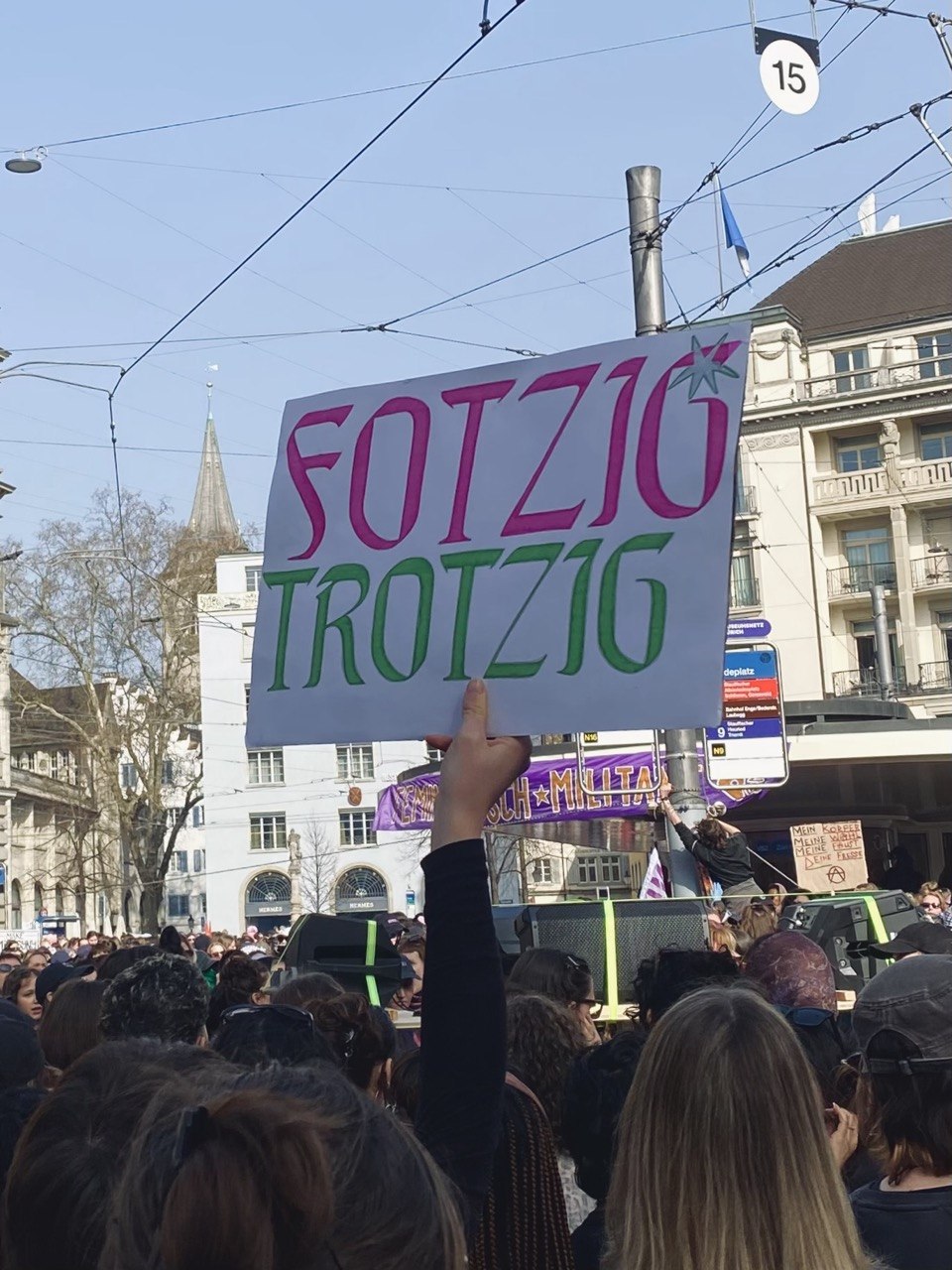 ein plakat wird wird in einer menge von menschen erhoben darauf steht fotzig und trotzig in pink grüner schrift